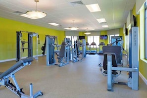 Ein Fitnessraum mit verschiedenen Trainingsgeräten, einem Fernseher und einer leuchtend gelben Wand.
