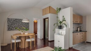 A modern kitchen with wooden cabinets, a dining area with a round table and chairs, and a living space with a large plant. - Palheiro 360 – Stunning Bay View (Funchal)
