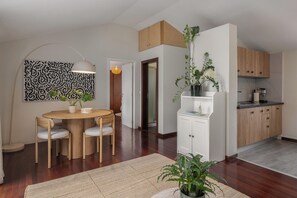Eine moderne Küche mit Holzausstattung, ein Essbereich mit rundem Tisch und Stühlen sowie ein Wohnbereich mit einer großen Pflanze.