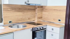 Una cocina moderna con armarios blancos, protector contra salpicaduras de madera, un lavamanos de acero inoxidable, horno empotrado y una placa de inducción negra.