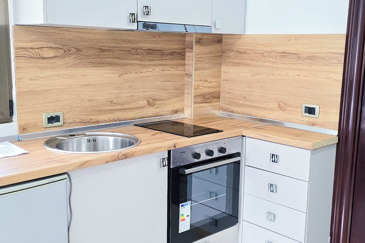 A modern kitchen with white cabinets, a wooden backsplash, a stainless steel sink, a built-in oven, and a black induction cooktop.