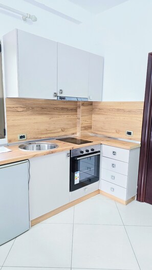 Una cocina moderna con armarios blancos, protector contra salpicaduras de madera, un lavamanos de acero inoxidable, horno empotrado y una placa de inducción negra.