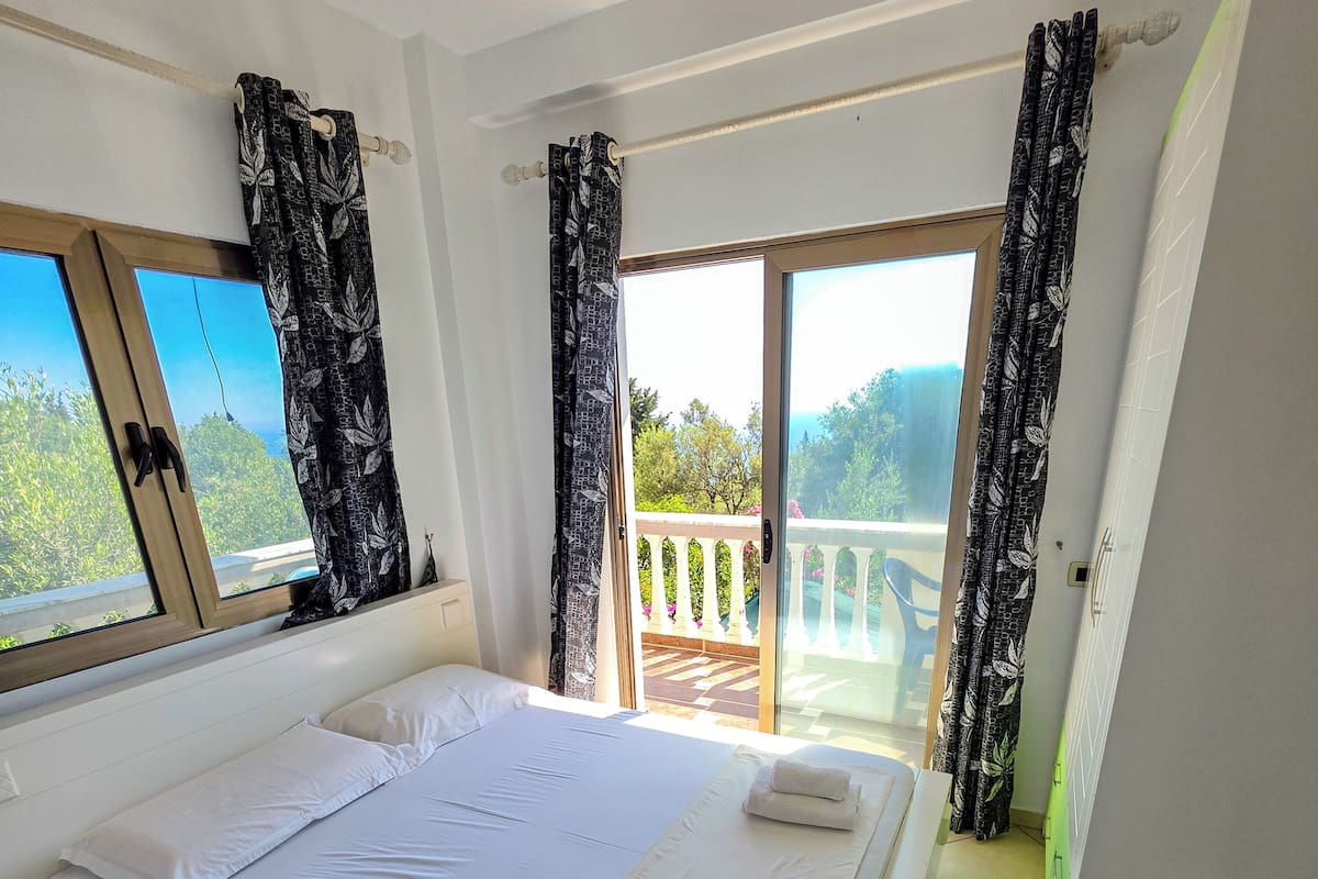A bedroom with a large bed, a balcony with a view, and a sliding glass door.