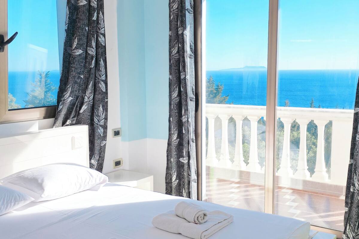 A bedroom with a bed, curtains, and a balcony with a view.