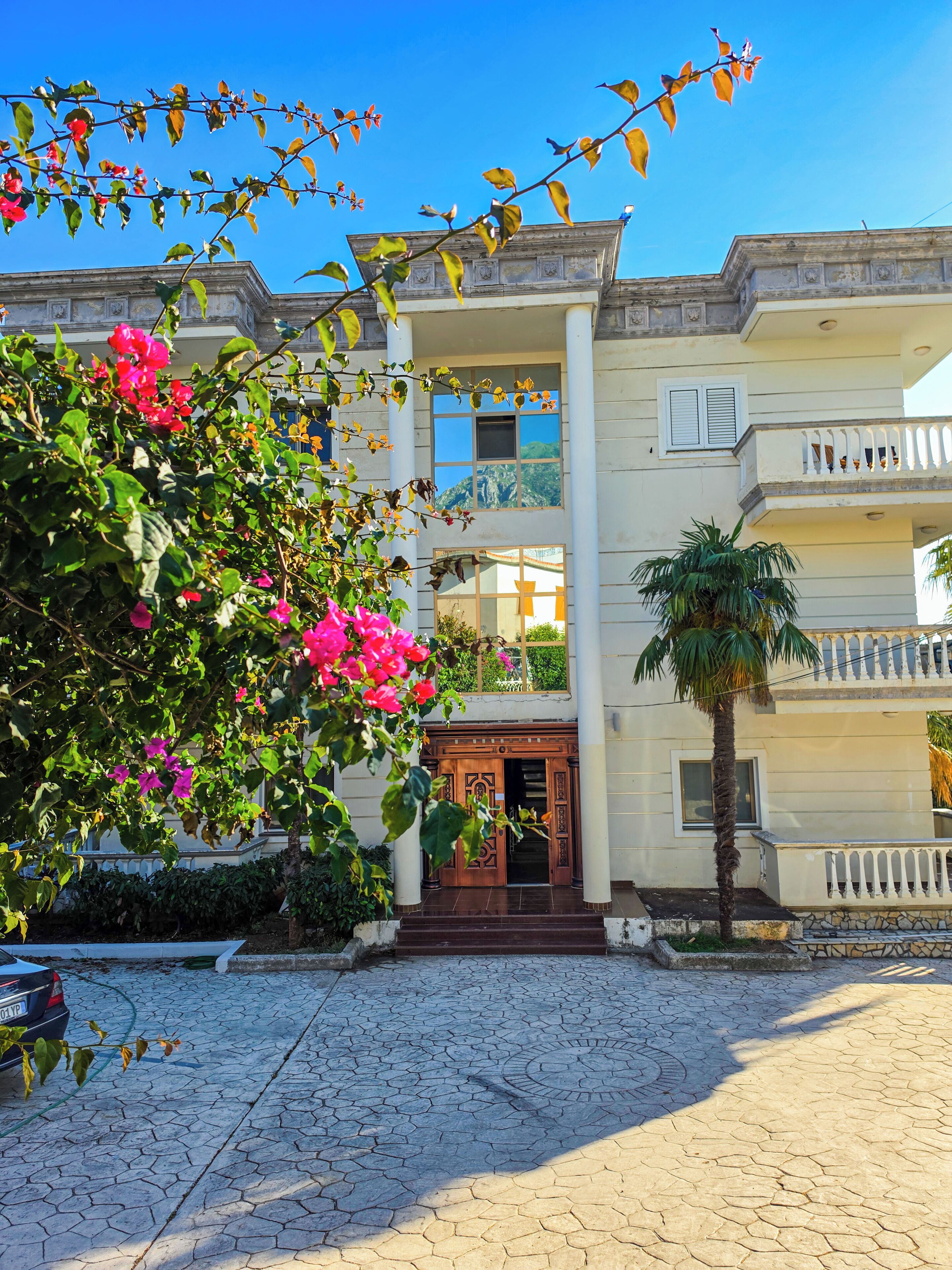 A two-story building with a central entrance, balconies, and a garden area.