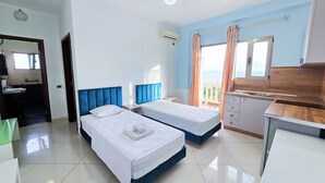 Habitación de hotel con dos camas, un baño, una kitchenette y un balcón con vistas.