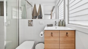 Et moderne badeværelse med et glasbadeværelsesafskærmning, et hvidt toilet, en trævasketømmefløj med vask og et spejl over vasketømmefløjen.