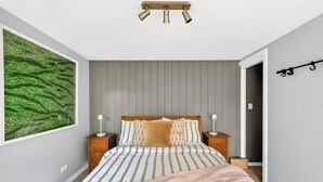 Et soveværelse med en seng, sengeborde, en vægmonteret lampe og et stort maleri.