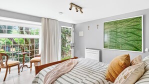 Et soveværelse med en stor seng, grønne omgivelser i vinduet, et lille bord og en stol.