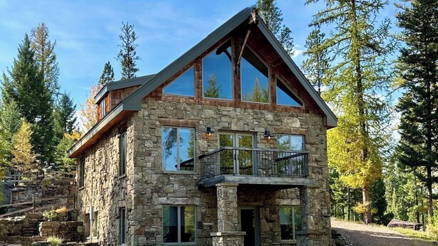 A stone cabin with a balcony, large windows, and a stone staircase. - Serene 4-bedroom house in Seeley Lake perfect for relaxing stays (Seeley Lake)