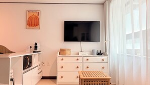 A modern hotel room with a flat-screen TV, a washing machine, a small wooden stool, and a bookshelf with books. - Modern Studio Near Gimpo Airport, King Bed + Pull-Out Trundle + Washer & Dryer (Seoul)