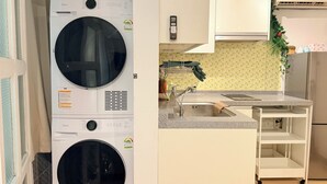 A compact kitchen with a built-in washer and dryer, a sink, and a small white shelf unit. - Modern Studio Near Gimpo Airport, King Bed + Pull-Out Trundle + Washer & Dryer (Seoul)