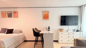 A modern hotel room with a bed, desk, chair, TV, and a wall with framed artwork. - Modern Studio Near Gimpo Airport, King Bed + Pull-Out Trundle + Washer & Dryer (Seoul)