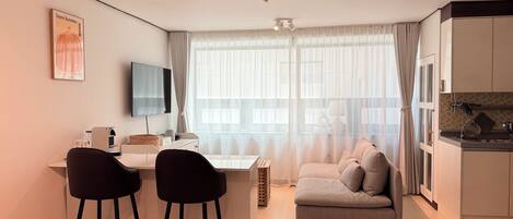 Una habitación de hotel moderna con escritorio, dos sillas, sofá, televisor y una zona de cocina.