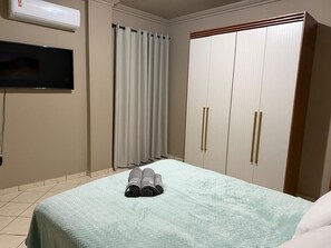 Quarto com cama, televisão, guarda-roupa e cortina.