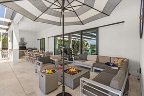 Un espace de vie extérieur moderne, doté d’un foyer, de sièges et d’un grand parasol.