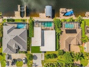 A modern building with a swimming pool, a covered outdoor area, and a parking lot. - Luxury Gulf Access Escape with Pool, Spa, Dock & Firepit Retreat - Villa Sogno - Roelens (Cape Coral)