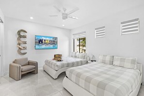 A modern bedroom with a large bed, a sofa, a TV, and a ceiling fan. - Luxury Gulf Access Escape with Pool, Spa, Dock & Firepit Retreat - Villa Sogno - Roelens (Cape Coral)