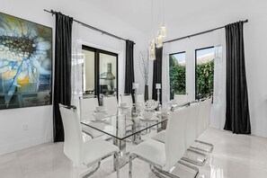 A modern dining room with a glass table, white chairs, and black curtains. - Luxury Gulf Access Escape with Pool, Spa, Dock & Firepit Retreat - Villa Sogno - Roelens (Cape Coral)