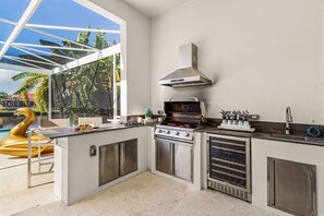 Eine moderne Küche mit integriertem Grill, Edelstahlgeräten und Blick auf einen Swimmingpool.