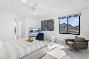 Een moderne slaapkamer met een bed, een blauwe stoel, een grijze bank, een televisie en een groot raam.
