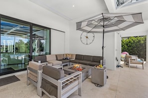 Een moderne woonkamer met een hoekbank, een glazen wand en een grote parasol.