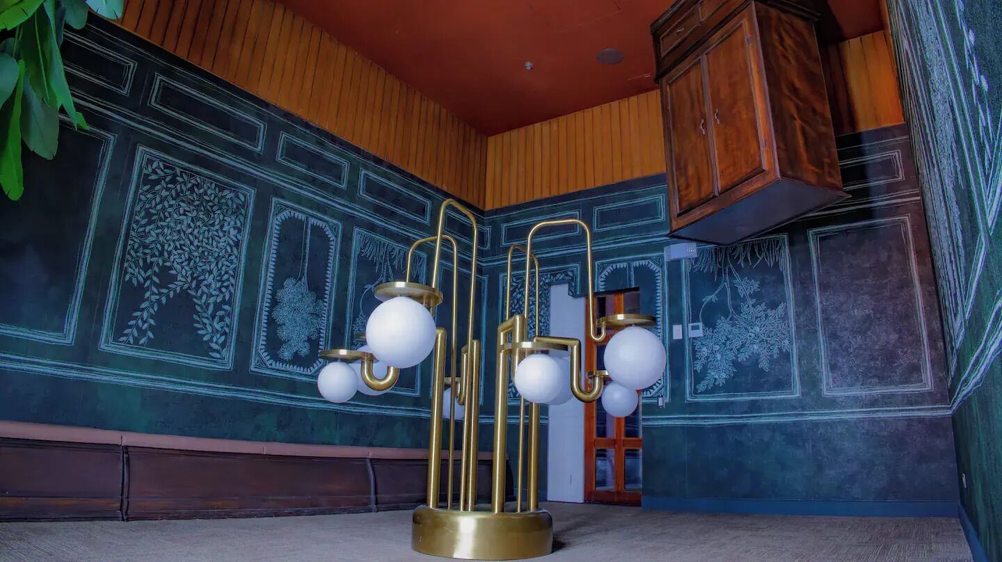 A room with a patterned wall, a wooden cabinet, and a floor lamp.