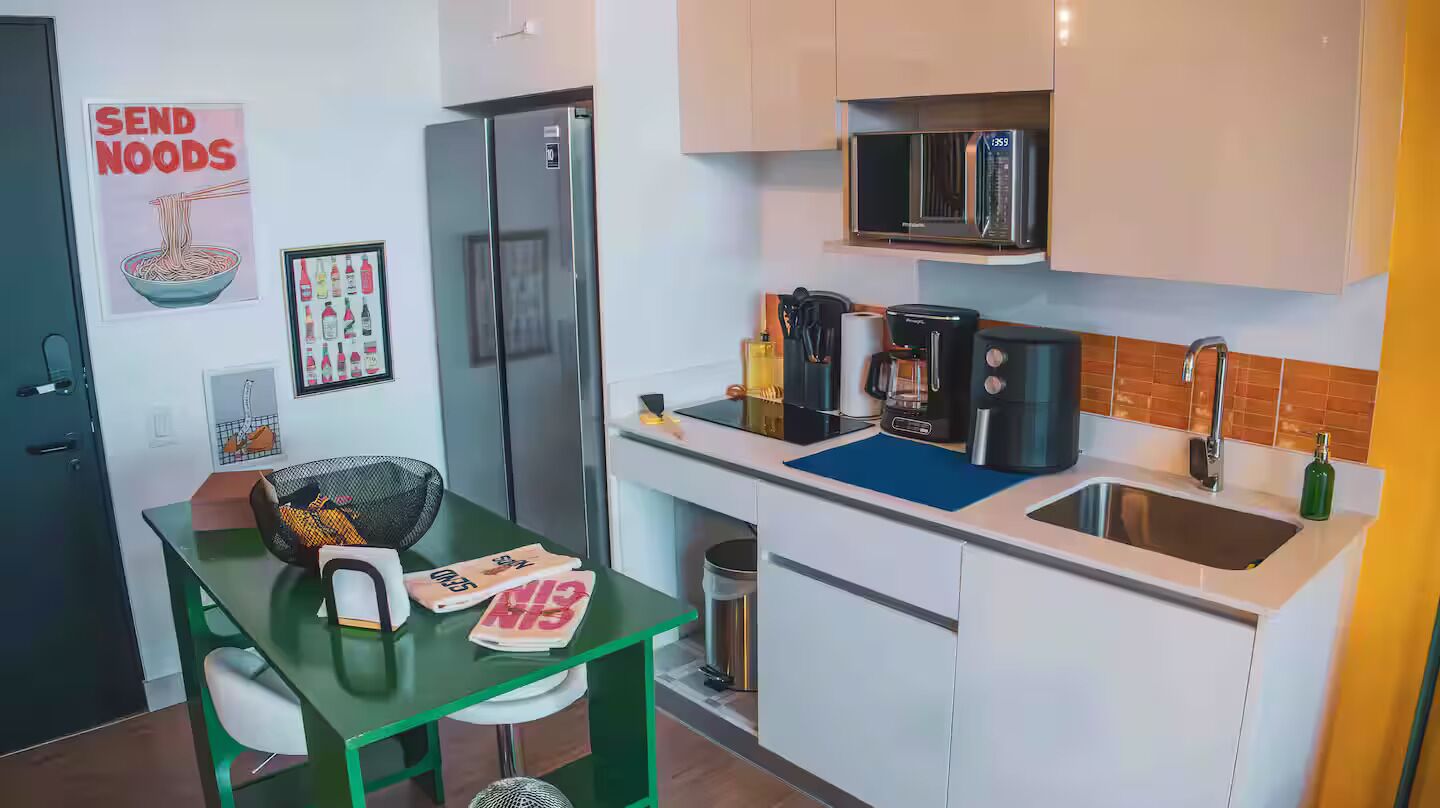 Een kleine keuken met een koelkast, magnetron, koffiezetapparaat en spoelbak.
