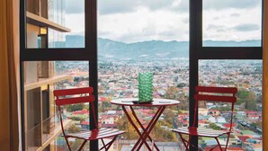 A room with a large window, two red chairs, a small round table, and a green vase.