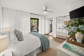 Ein modernes Schlafzimmer mit Bett, Vorhängen, Deckenventilator, Fernseher, Pflanze und Bücherregal.
