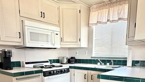 Une cuisine de taille réduite, avec des meubles blancs, un four à micro-ondes, une cuisinière et une poubelle.