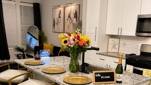 En köksö med barstolar, en välkomstskylt, en vas med blommor och en flaska champagne.