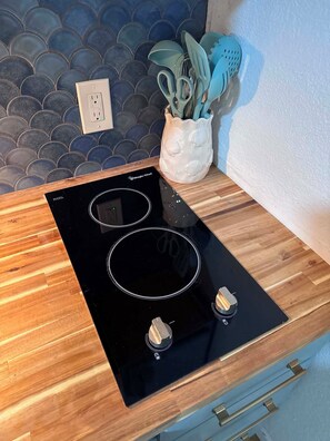 Una cocina con tope de inducción negro, encimera de madera y un salpicadero decorativo.