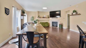 A dining area with a wooden table and chairs, a sofa, a television, and a fireplace.