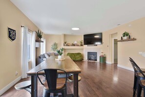 A dining area with a wooden table and chairs, a sofa, a television, and a fireplace.