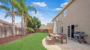 A backyard with a patio, a wooden table, a bench, a grill, and a wooden fence.