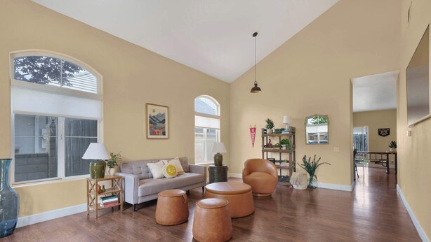 A spacious living room with a sofa, ottomans, a coffee table, a lamp, and a bookshelf.
