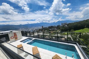 Ein Pool auf dem Dach mit Blick auf die Stadt, einer Glasbrüstung und wolkenlosem Himmel.