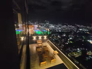 Ein Hotelzimmer in einem Hochhaus mit Blick auf die Stadt, einem Sitzbereich auf dem Balkon und einem großen Fenster.
