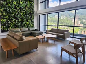 Ein modernes Wohnzimmer mit einem Ecksofa, einem runden Couchtisch und Blick auf eine Stadtlandschaft durch große Fenster.