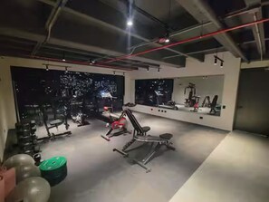 Ein Fitnessraum mit Trainingsgeräten, einem großen Spiegel und Blick auf die beleuchtete Stadt.