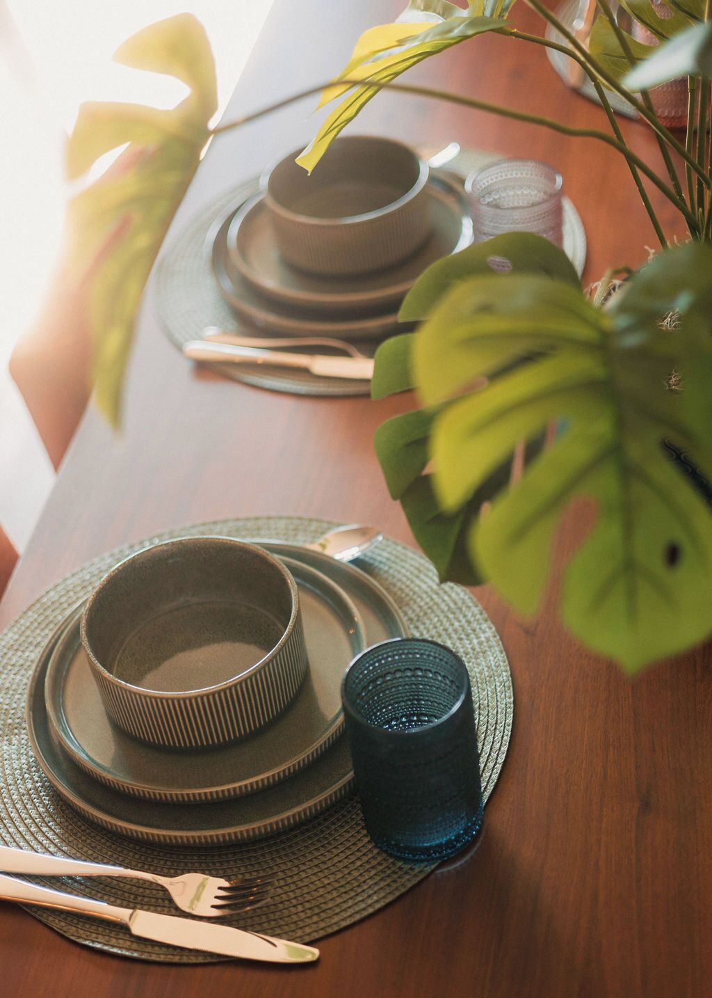 Una mesa de comedor dispuesta con platos, tazones y cubiertos, con una planta de fondo.