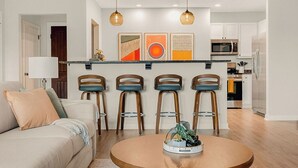 Een moderne woonkamer met een ronde houten salontafel, een bank en een keukenbar met een barkruk.