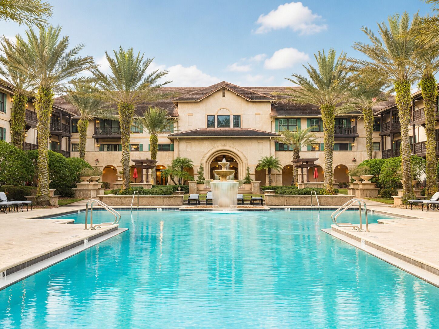 A hotel with a central pool, palm trees, and a fountain.