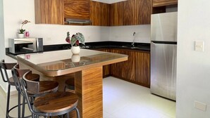Eine moderne Küche mit Holzschränken, einem Edelstahlkühlschrank und einer Kücheninsel mit Glasausstattung und Barhocker.