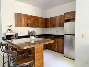 A modern kitchen with wooden cabinetry, a stainless steel refrigerator, and a glass island with bar stools. - Torre Toronto Zona Dorada by GPS (Mazatlán)