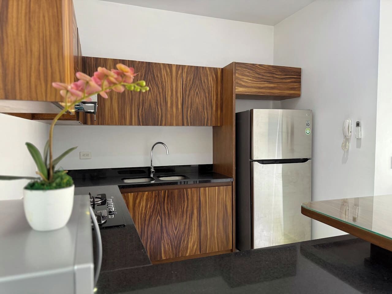 A modern kitchen with wooden cabinets, a stainless steel refrigerator, a sink, and a potted plant.