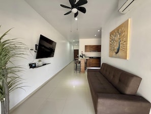 A modern living room with a flat-screen TV, a ceiling fan, a brown sofa, a dining area, and a kitchen in the background. - Torre Toronto Zona Dorada by GPS (Mazatlán)