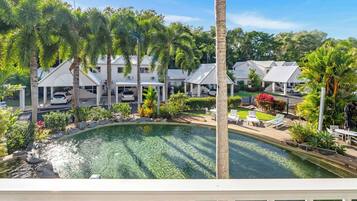 A pool with a curved edge, surrounded by palm trees and a white building with a covered carport.