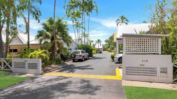 A residential street with houses, palm trees, and a gated entrance.
